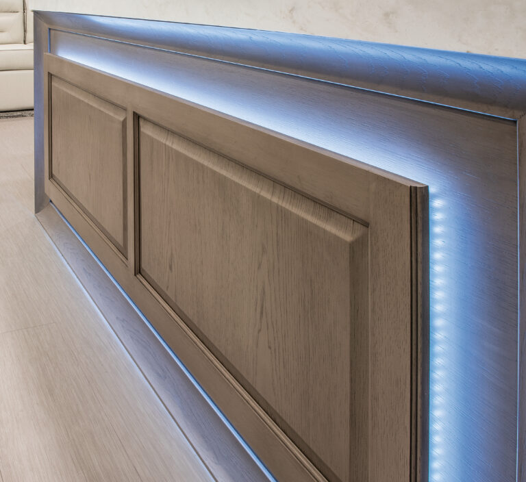 A close-up of a wooden panel with a geometric pattern, accentuated by blue LED lighting along the top edge, exudes the refined ambiance typical of luxury RVs. Resting against a light-colored floor, it creates a modern and sleek interior design aesthetic.