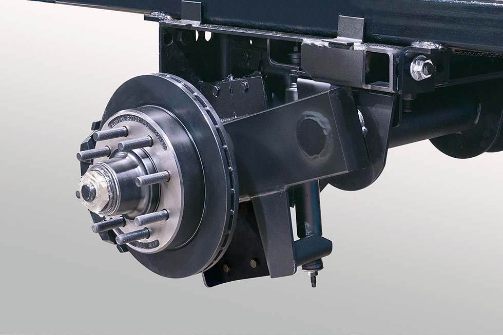 Close-up of a vehicle braking system, highlighting the drum brake and suspension components. The metal parts are mounted on a black chassis, showing intricate mechanical details against a neutral background.